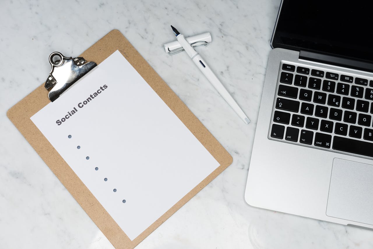 Minimalist workspace featuring a clipboard, laptop, and pen on a marble surface.